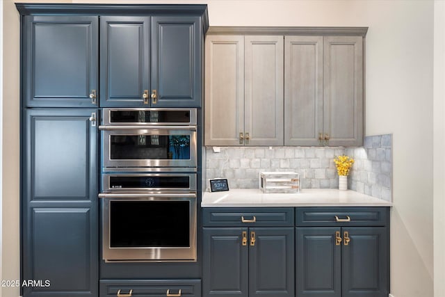 kitchen with backsplash, blue cabinets, double oven, and light countertops