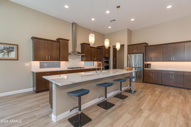 kitchen featuring a breakfast bar, stainless steel appliances, visible vents, a sink, and wall chimney range hood