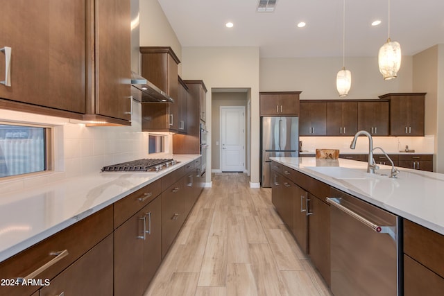 kitchen featuring stainless steel appliances, visible vents, decorative backsplash, a sink, and wall chimney exhaust hood