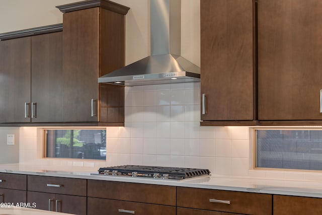 kitchen featuring dark brown cabinetry, decorative backsplash, wall chimney exhaust hood, light countertops, and stainless steel gas cooktop