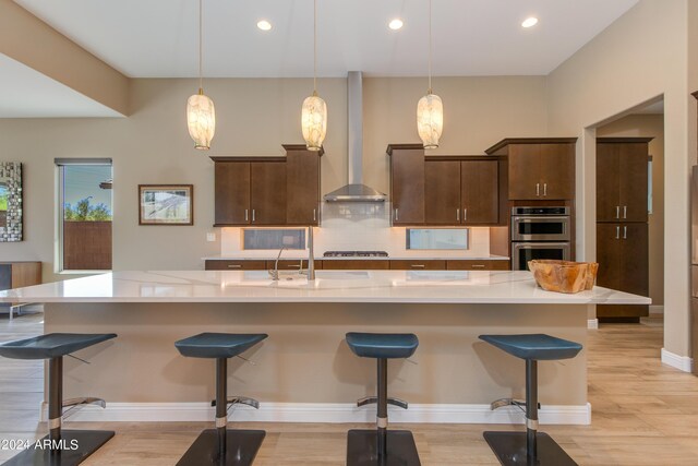 kitchen featuring backsplash, light hardwood / wood-style floors, wall chimney range hood, and double oven