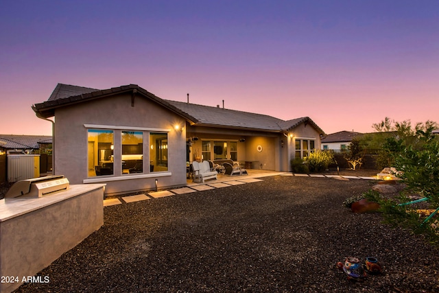 back of house at dusk featuring an outdoor kitchen, a tile roof, fence, a patio area, and stucco siding