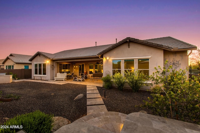 back of house at dusk featuring a patio, ceiling fan, a tiled roof, fence, and stucco siding