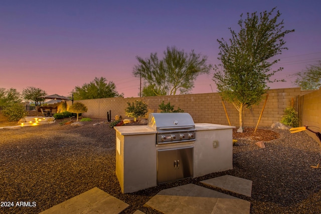 patio terrace at dusk with a grill, a fenced backyard, and area for grilling