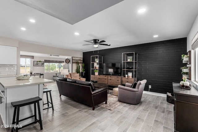 living room featuring ceiling fan, brick wall, and light wood-type flooring