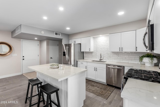 kitchen featuring stainless steel appliances, sink, white cabinetry, light hardwood / wood-style flooring, and a kitchen island