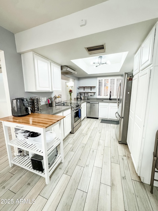 kitchen featuring wood counters, visible vents, white cabinets, appliances with stainless steel finishes, and a tray ceiling