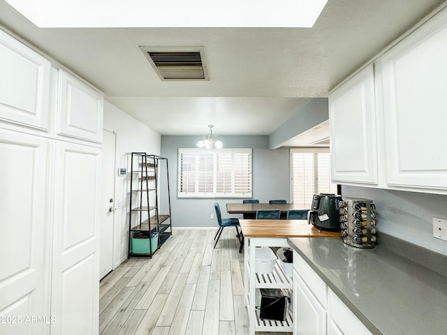 kitchen featuring a notable chandelier, visible vents, white cabinets, light wood-type flooring, and dark countertops