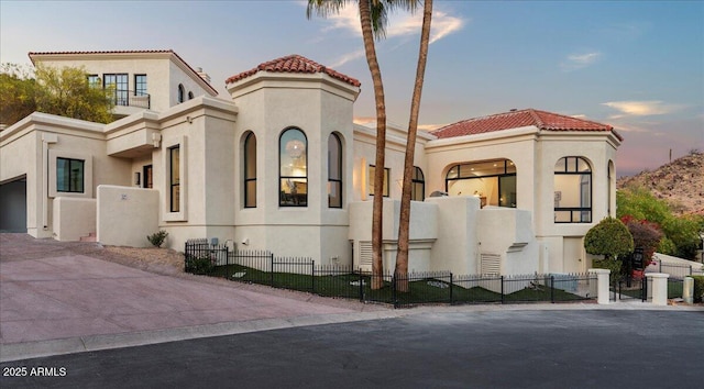 mediterranean / spanish house with a fenced front yard, stucco siding, and a tile roof