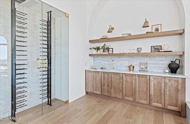 bar featuring tasteful backsplash, light wood-style flooring, a sink, and indoor wet bar