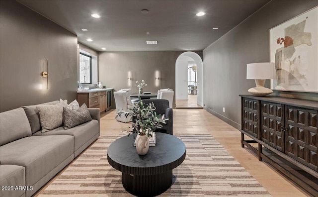 living room with visible vents, baseboards, arched walkways, light wood-style floors, and recessed lighting