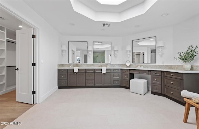 full bathroom featuring vanity, baseboards, a walk in closet, visible vents, and wood finished floors