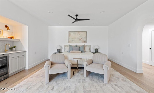 bedroom featuring baseboards, arched walkways, a sink, light wood-style floors, and beverage cooler