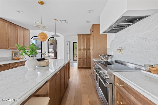 kitchen with brown cabinetry, light wood-style flooring, wall chimney range hood, visible vents, and range with two ovens