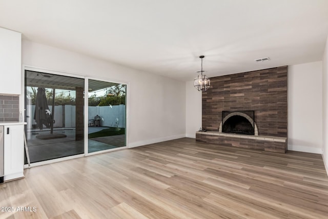 unfurnished living room with baseboards, visible vents, an inviting chandelier, light wood-style floors, and a large fireplace