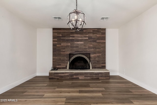 unfurnished living room featuring an inviting chandelier, a brick fireplace, wood finished floors, and visible vents