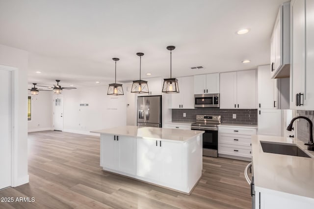 kitchen with visible vents, a sink, a kitchen island, stainless steel appliances, and decorative backsplash