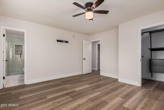 unfurnished bedroom featuring a walk in closet, baseboards, and wood finished floors