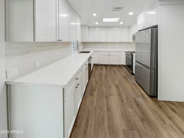 kitchen with light hardwood / wood-style floors, tasteful backsplash, white cabinets, stainless steel appliances, and sink