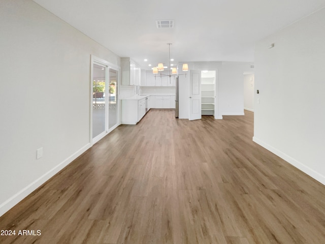 unfurnished living room with light wood-type flooring and a notable chandelier