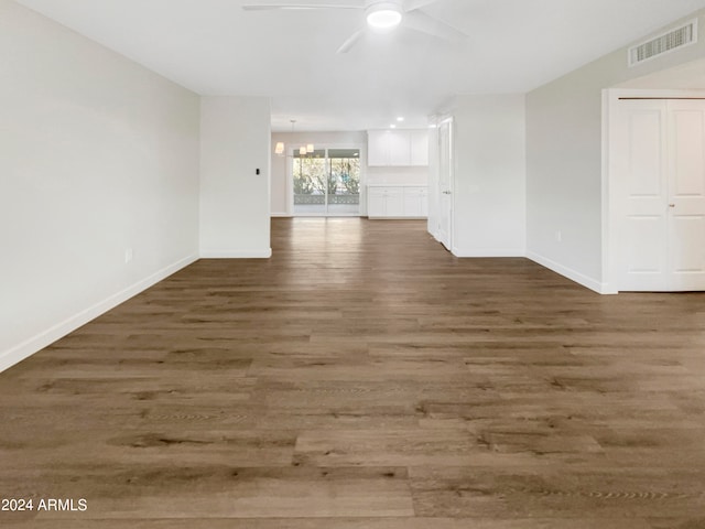 unfurnished living room featuring ceiling fan with notable chandelier and dark wood-type flooring