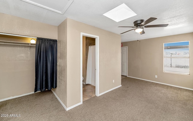 unfurnished bedroom with ceiling fan, a skylight, baseboards, and carpet