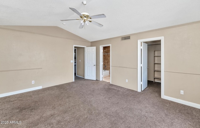 unfurnished bedroom with a walk in closet, visible vents, carpet floors, lofted ceiling, and ensuite bathroom