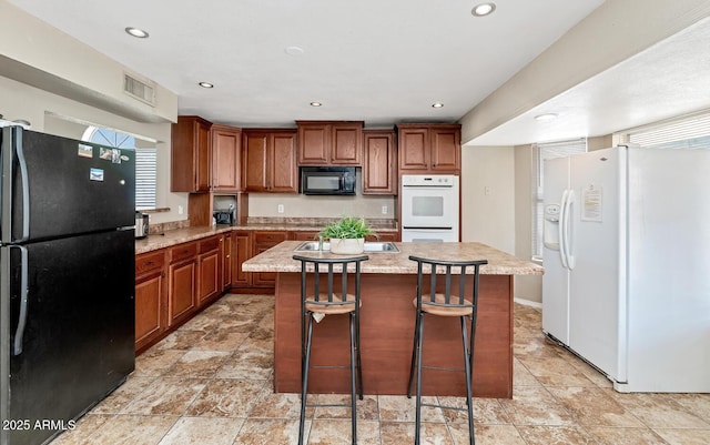 kitchen featuring brown cabinetry, recessed lighting, a kitchen island, visible vents, and black appliances