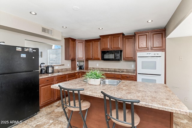 kitchen featuring light countertops, brown cabinetry, visible vents, a center island with sink, and black appliances