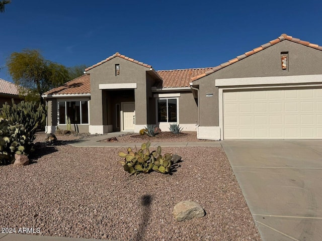 mediterranean / spanish house with a garage, a tiled roof, concrete driveway, and stucco siding