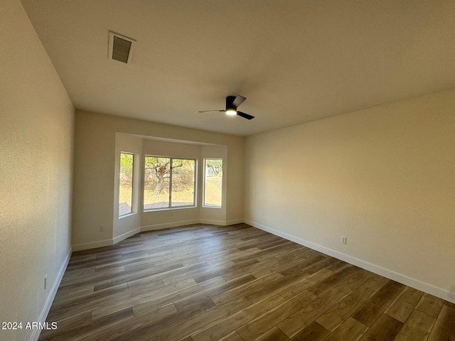 spare room with ceiling fan, wood finished floors, visible vents, and baseboards