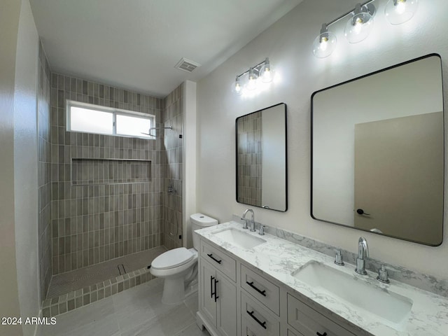 bathroom with a tile shower, vanity, toilet, and tile patterned floors