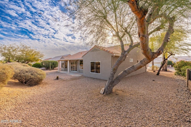 back of house with stucco siding, a tiled roof, and a patio