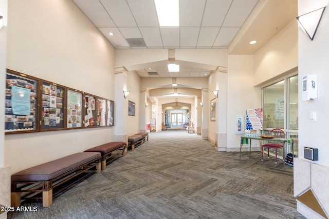 hallway featuring arched walkways, a paneled ceiling, recessed lighting, a towering ceiling, and baseboards