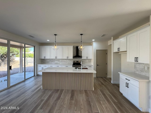 kitchen with light countertops, wall chimney range hood, a center island with sink, and white cabinets