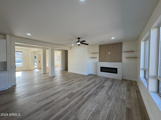 unfurnished living room with a tile fireplace, ceiling fan, and wood-type flooring