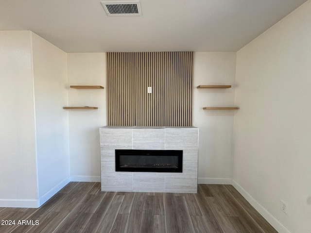 unfurnished living room featuring dark wood-style flooring, a tiled fireplace, visible vents, and baseboards