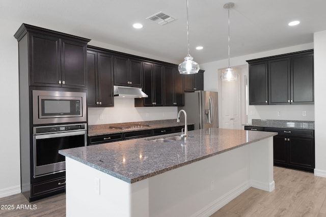 4853 N 183rd Ln, Goodyear, AZ 85395 - kitchen featuring stainless steel appliances, a sink, light wood finished floors, dark stone counters, and under cabinet range hood