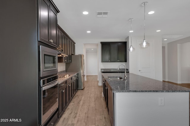4853 N 183rd Ln, Goodyear, AZ 85395 - kitchen featuring appliances with stainless steel finishes, a sink, a kitchen island with sink, dark stone countertops, and light wood-style flooring