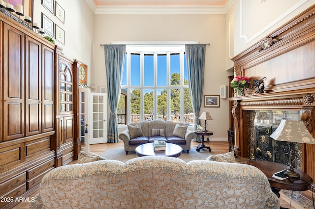 living area featuring wood finished floors, a high end fireplace, a high ceiling, crown molding, and baseboards