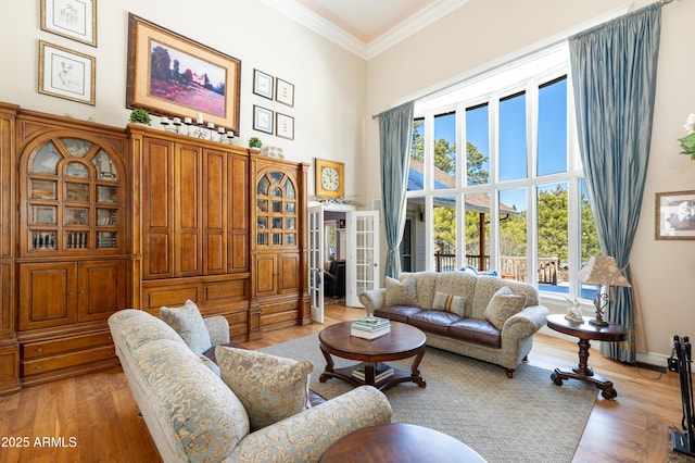 living room with light wood-style floors, baseboards, crown molding, and a high ceiling