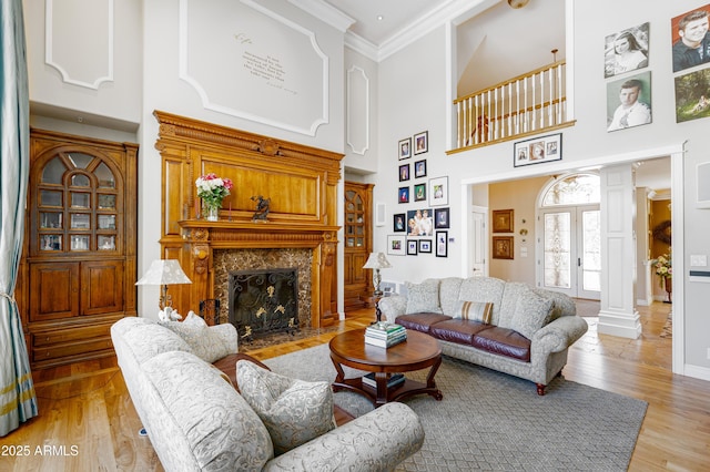 living room featuring light wood finished floors, crown molding, baseboards, a premium fireplace, and ornate columns