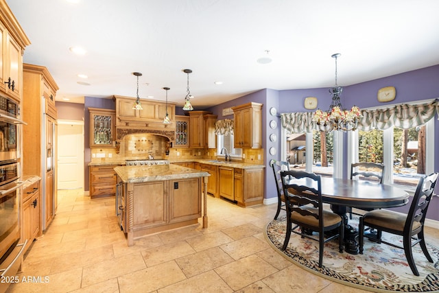 kitchen with a notable chandelier, decorative backsplash, a kitchen island, glass insert cabinets, and light stone countertops