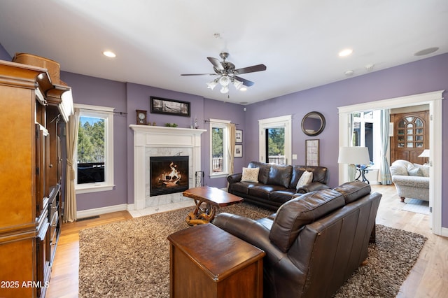 living room featuring a wealth of natural light, ceiling fan, a high end fireplace, and light wood finished floors