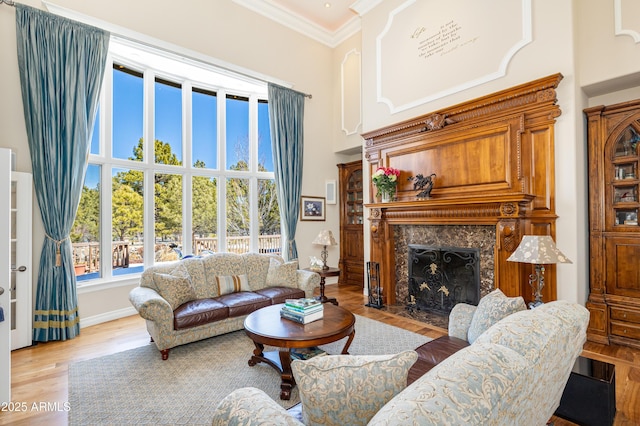living area with a high ceiling, ornamental molding, a fireplace, and light wood finished floors
