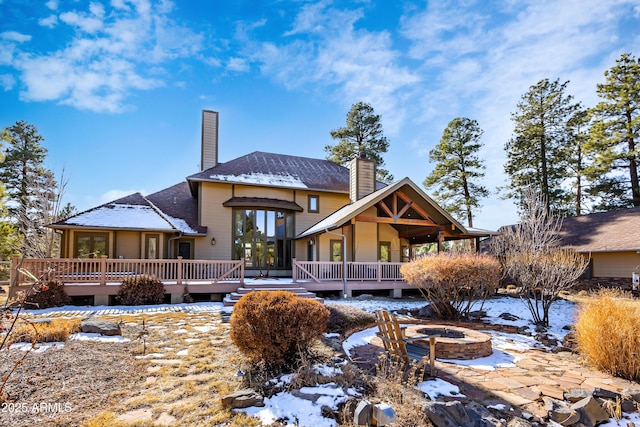 snow covered rear of property featuring a deck, a chimney, and an outdoor fire pit