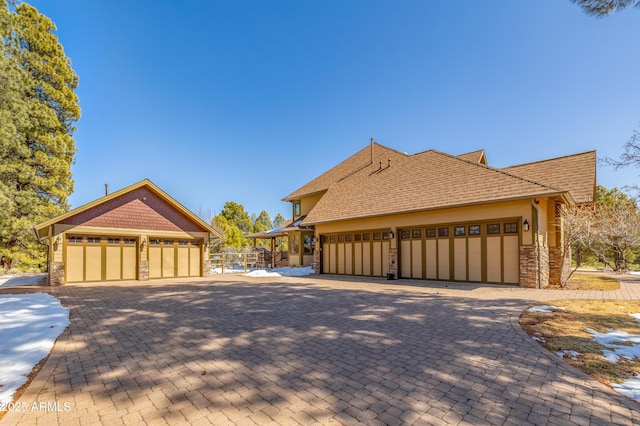 view of side of home featuring stone siding, a shingled roof, and decorative driveway