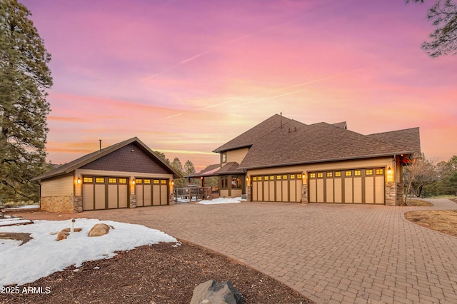 view of front facade with decorative driveway, stone siding, a garage, and roof with shingles