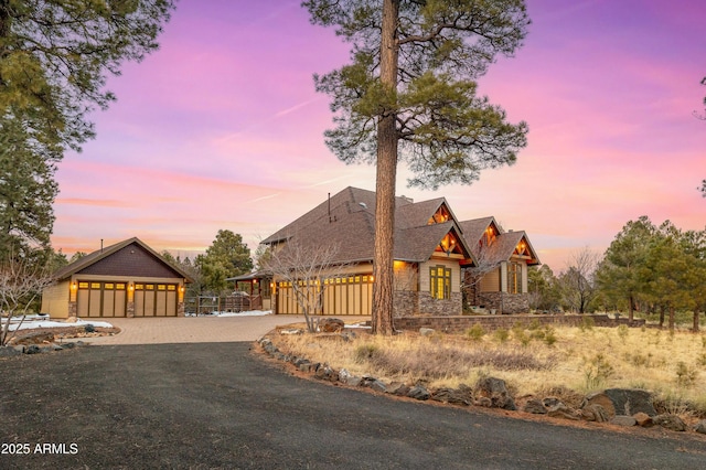view of front of property featuring stone siding, driveway, and fence