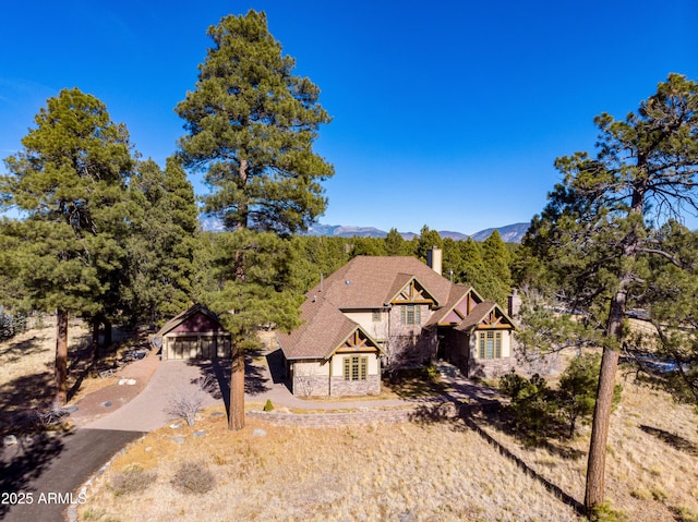 english style home with stone siding, a mountain view, driveway, and a chimney